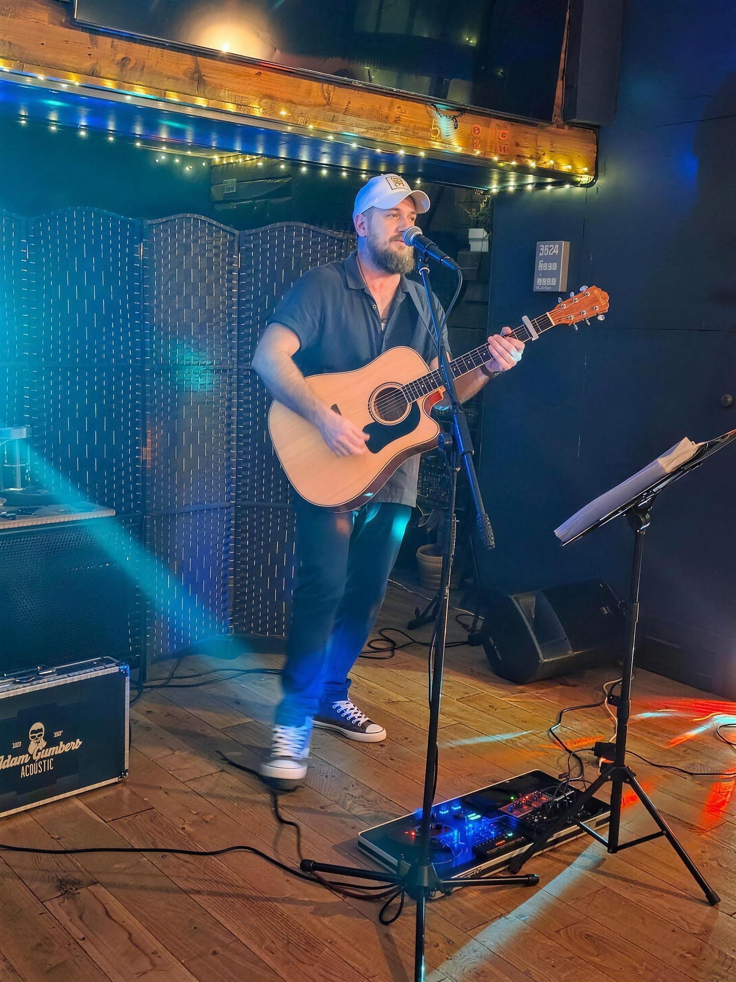 Solo acoustic singer-guitarist playing on the bar room floor under fairy lights
