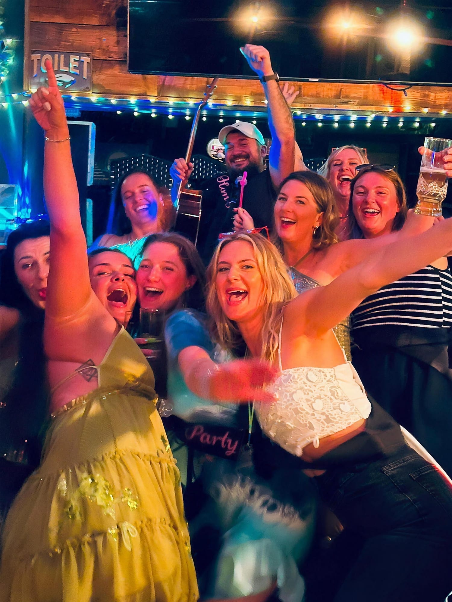 A hen party celebrating with a solo acoustic guitarist performing behind them
