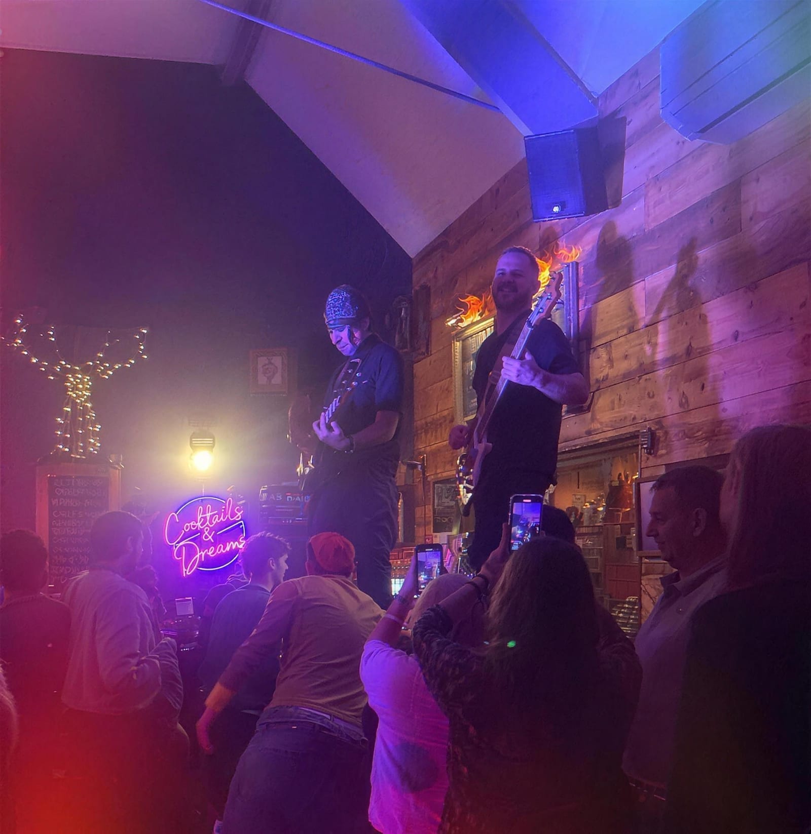 A live band playing to a packed crowd in front of the neon Cocktails & Dreams sign